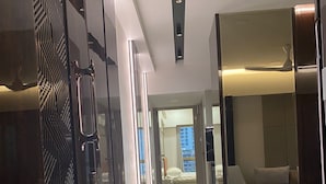 A modern hotel corridor with a marble floor, a glass door with a geometric pattern, and a view into a room with a bed and a cityscape. - Southside by Daily Stays (Mumbai)