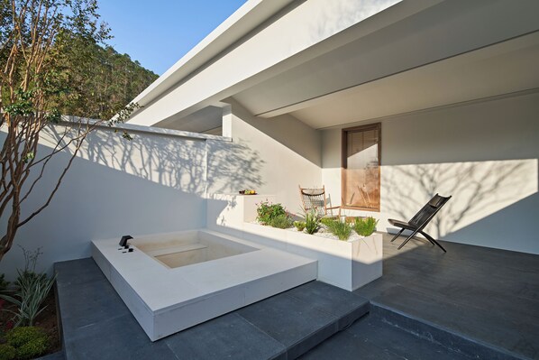 A modern outdoor patio with a rectangular hot tub, a wooden door, and a black chair.