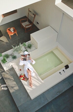 A modern outdoor relaxation area with a hot tub, a wooden rocking chair, and a small table with a bowl of fruit and a book. - Even's Garden (Huizhou)