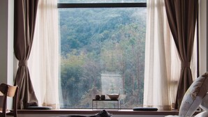 Una camera da letto con una grande finestra, un letto, una sedia e un tavolino con due tazze.