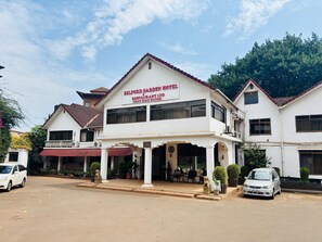 A two-story building with a sign for Belford Garden Hotel and Restaurant Ltd. It features a balcony, a covered entrance, and a parking area in front. - FANG FANG SUITES (Kampala)