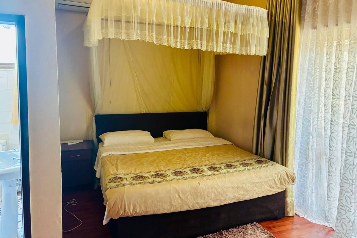 Een net opgemaakt bed met hemelbed, nachtkastje en nachttafel.