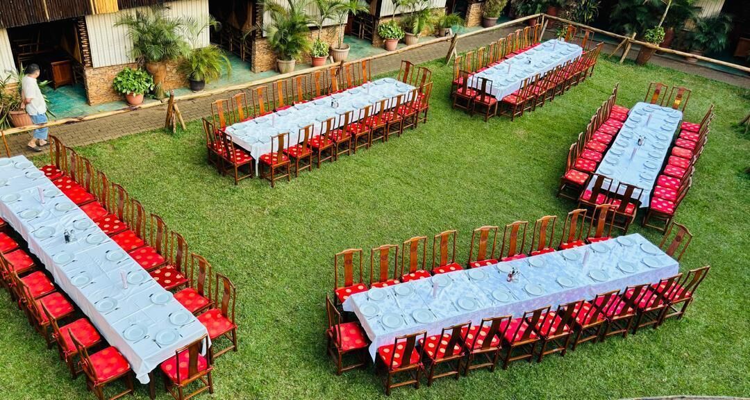 Un área de comedor al aire libre con varias mesas largas dispuestas sobre un césped, rodeada de sillas de madera.