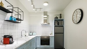 A modern kitchen with light blue cabinets, a white countertop, a built-in oven, a stainless steel refrigerator, and a wall-mounted clock. - Luxury A by OTOTO (Thessaloniki)