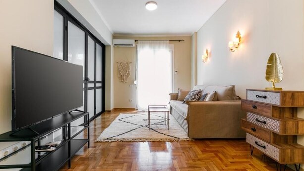 A modern living room with a flat-screen TV, a sofa, a wooden cabinet, and a patterned rug. - Luxury A by OTOTO (Thessaloniki)