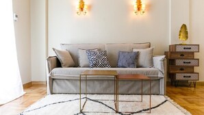 A living room with a sofa, patterned cushions, a small wooden side table, and a decorative plant. - Luxury A by OTOTO (Thessaloniki)