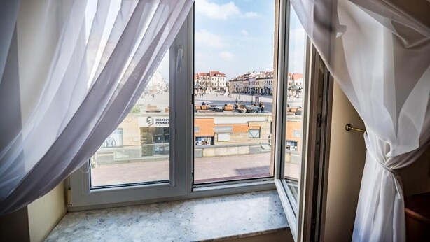 Une chambre d’hôtel avec une grande fenêtre, des rideaux blancs et une vue sur le paysage urbain.