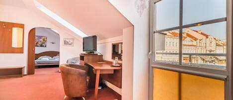 Habitación de hotel con cama, escritorio, silla, televisión y un amplio ventanal con vista a la ciudad.