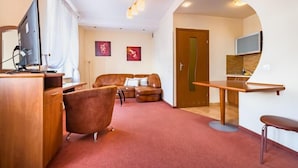 Un espace de vie compact comprenant un bureau en bois, un canapé en cuir, une télévision et une petite table à manger.