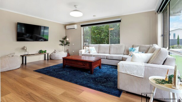 Een moderne woonkamer met een houten vloer, een groot raam, een bank, een salontafel en een aan de muur bevestigde televisie.