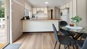 Een moderne keuken met een centraal eiland, een eethoek met een glazen tafel en uitzicht op het omliggende landschap.