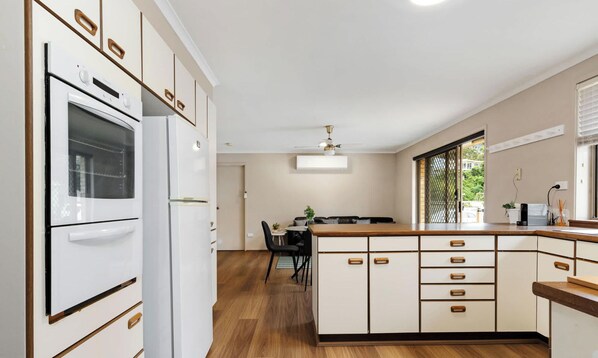 A kitchen with white cabinetry, a built-in oven, and a dining area with a table and chairs.