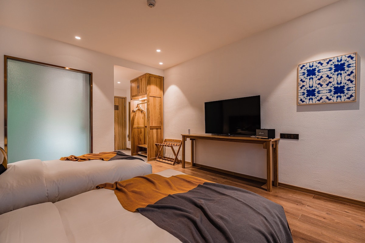 A modern hotel room with a bed, a TV, a wooden desk, and a blue patterned wall decoration.