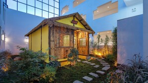 A small wooden cabin with a thatched roof, surrounded by a garden with stepping stones and plants. -  Lijiang Snow Mountain Bengu Hotel (Shuhe Ancient Town Branch) (Lijiang)