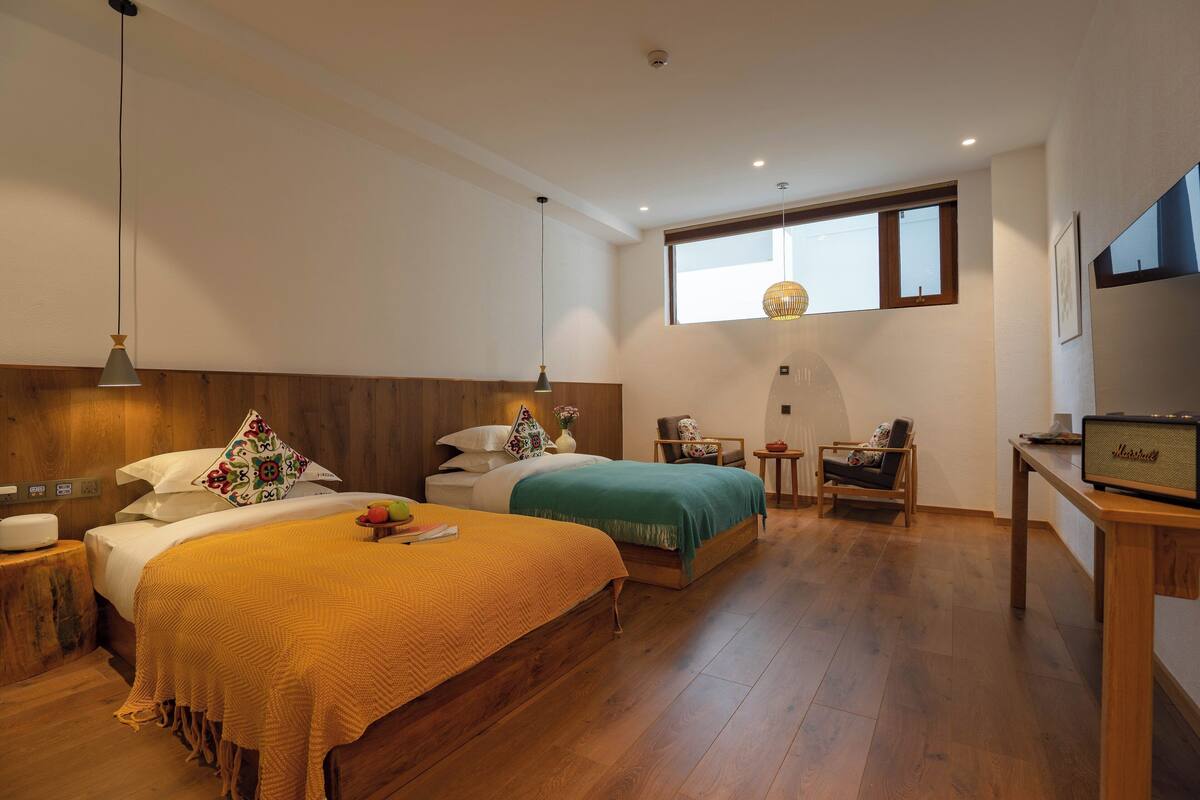 A bedroom with two beds, a wooden floor, a desk with a radio, and a window with a view.