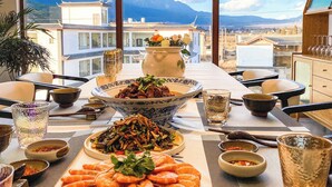 A dining table set with various dishes, including shrimp and a bowl of salad, in a room with a large window overlooking a mountainous landscape. -  Lijiang Snow Mountain Bengu Hotel (Shuhe Ancient Town Branch) (Lijiang)