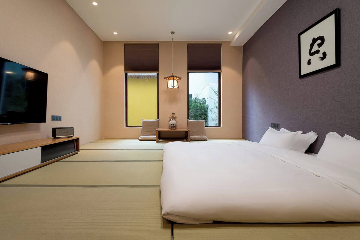 A modern hotel room with a large bed, a TV, a small table, and a sofa.