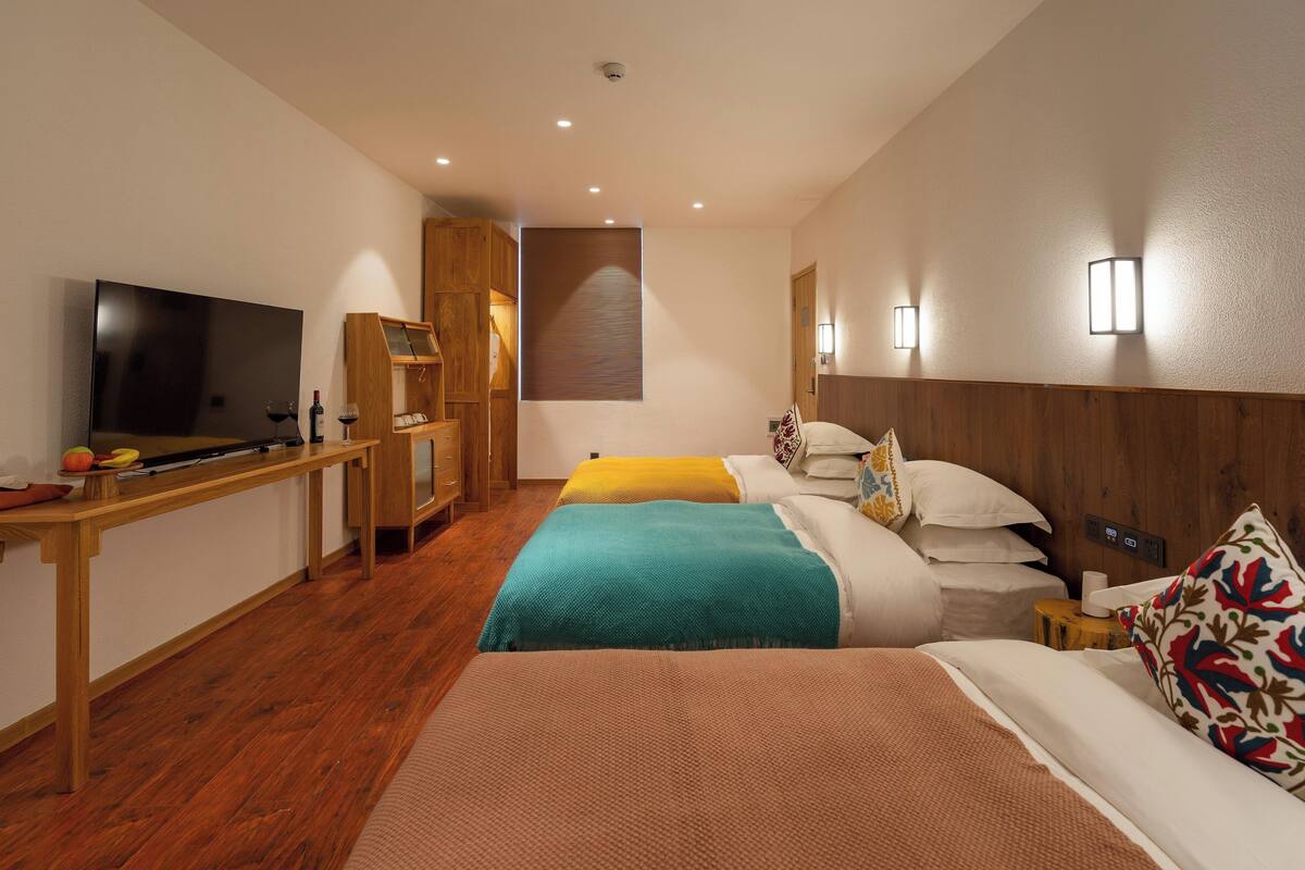 A hotel room with a TV, wooden desk, two beds, and a small table.