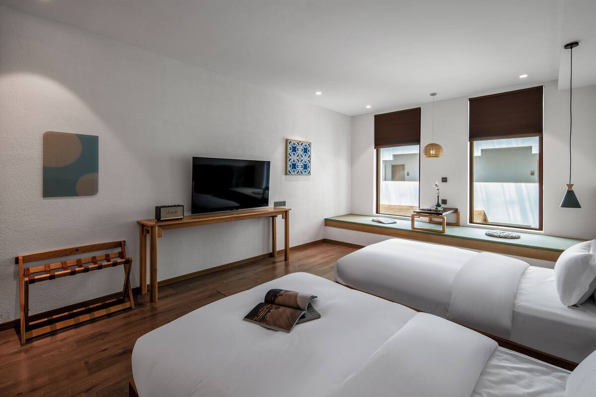 A modern hotel room with a large bed, a TV on a wooden stand, a small table, and a window with a view.