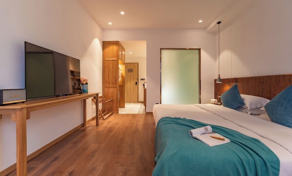 A modern hotel room with a wooden floor, a bed with teal bedding, a TV on a wooden desk, and a wooden wardrobe. - Lijiang Snow Mountain Bengu Hotel (Shuhe Ancient Town Branch) (Lijiang)