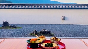 A table with various dishes in front of a wall with a traditional tiled roof and a mountain view. -  Lijiang Snow Mountain Bengu Hotel (Shuhe Ancient Town Branch) (Lijiang)