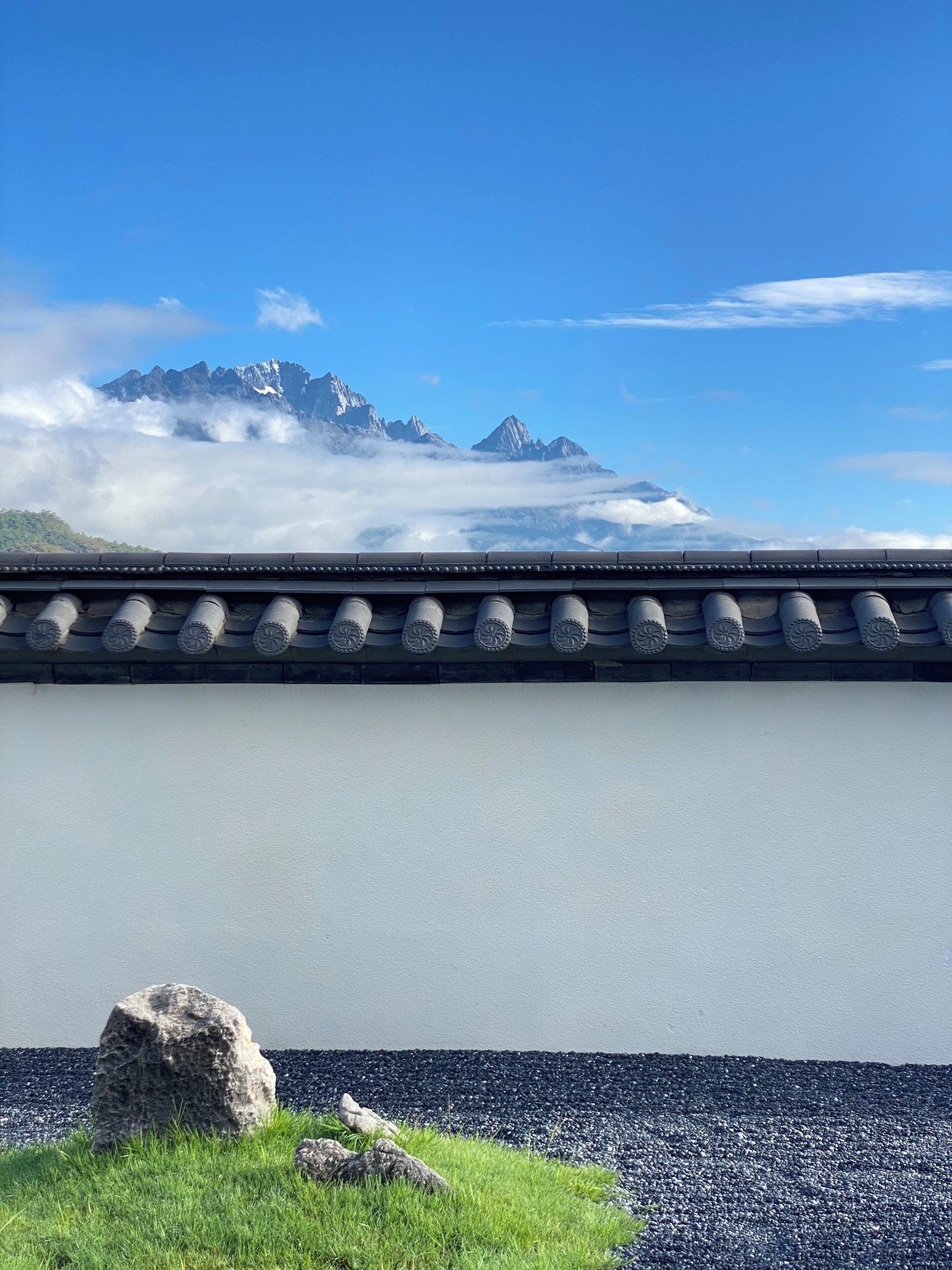 A traditional building with a tiled roof and a view of snow-capped mountains through clouds.