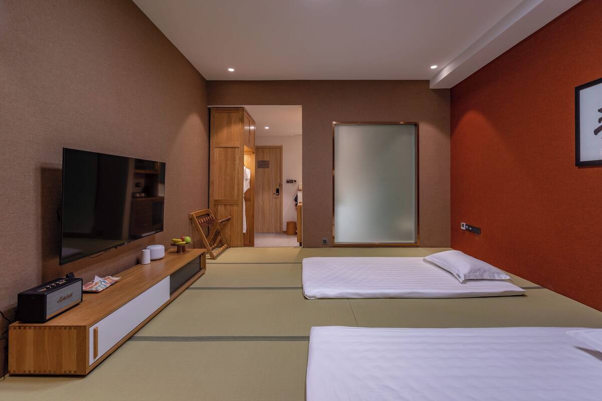 A hotel room with a TV, a wooden cabinet, a bed, and a futon.