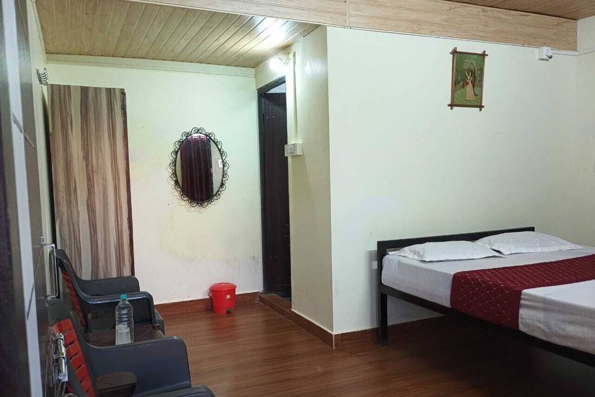 Hotellihuoneessa on sänky, tuoli, pieni pöytä, punainen ämpäri ja peili seinällä.