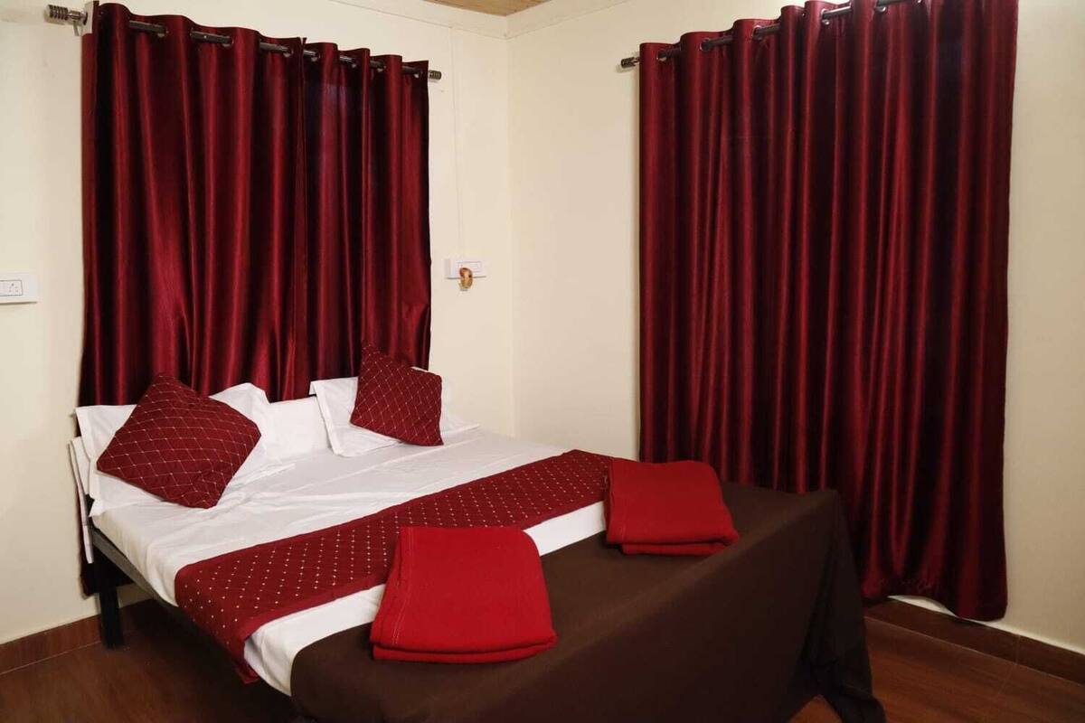 Hotellihuone, jossa on sänky, punaiset verhot ja ruskea peitto.