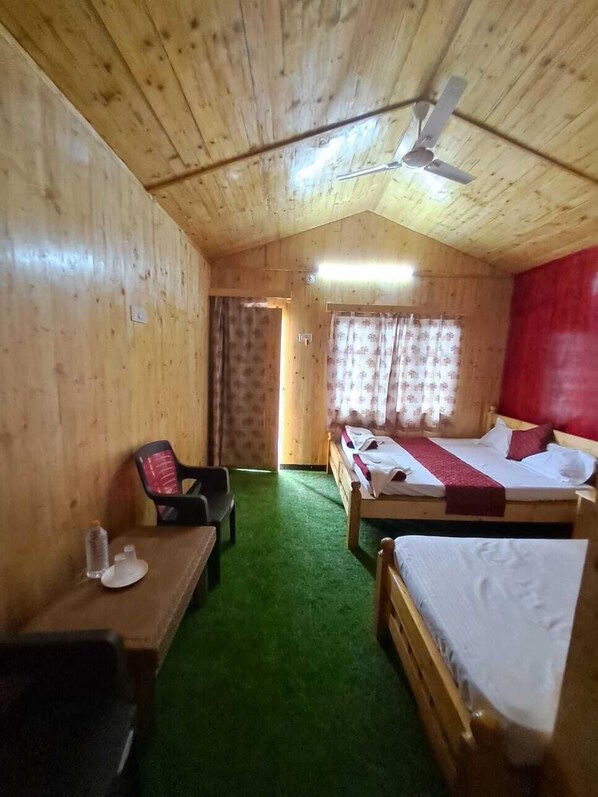 Habitación de cabaña de madera con dos camas, un escritorio, una silla y un ventilador de techo.