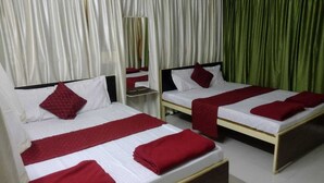 A hotel room with two single beds, each with a red blanket and pillow, white bedding, and a wooden headboard. - Cheetah Farms Jungle Stay (Haliyal)