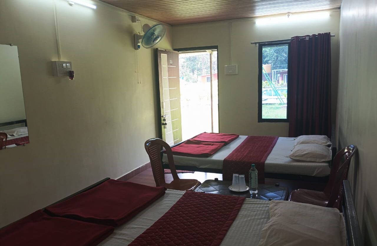 A room with two beds, a chair, a table with a bottle, and a window with curtains.