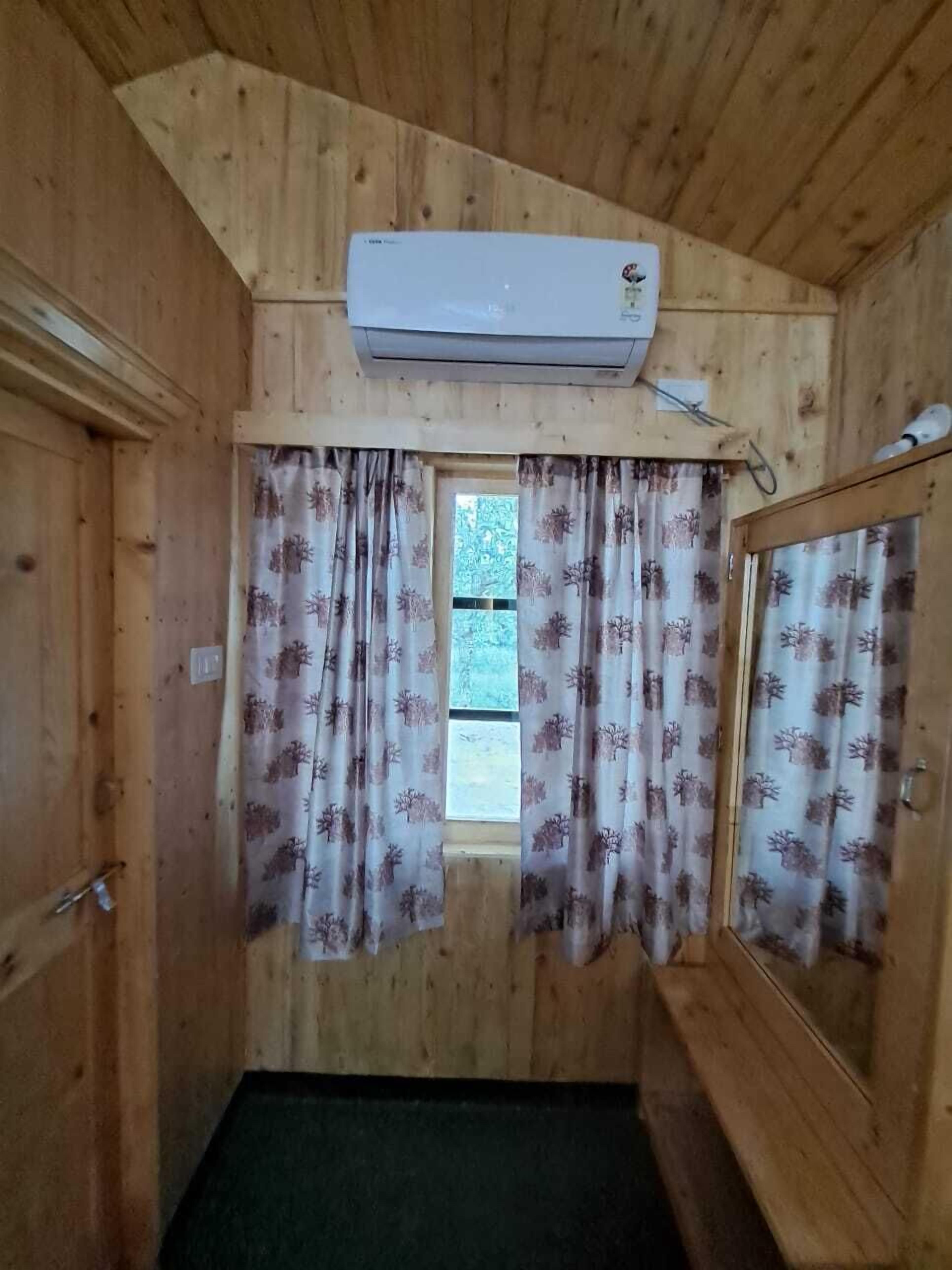 Una habitación de cabaña de madera con ventana, cortinas y un equipo de aire acondicionado.