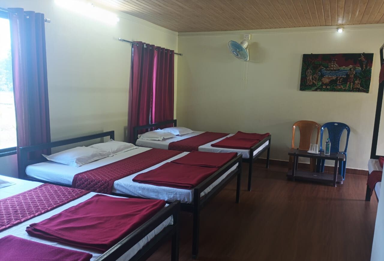 A room with three beds, each with red bedding, a wooden ceiling, and a wall-mounted fan.