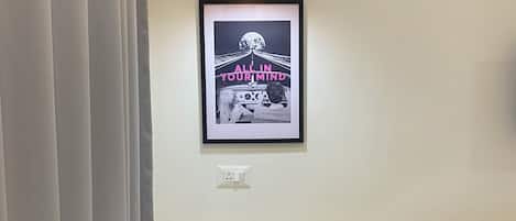 A room with a white table, a framed picture on the wall, a black chair, and a black speaker.