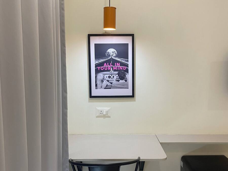 Una habitación con una mesa blanca, un cuadro en la pared, una silla negra y un altavoz negro.