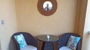 Ein kleiner Patio-Bereich mit zwei Korbstühlen und einem runden Tisch, mit einem runden Spiegel an der Wand.