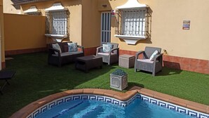 Ein Poolbereich mit gefliestem Rand, Gartenmöbeln und einem kleinen Garten.