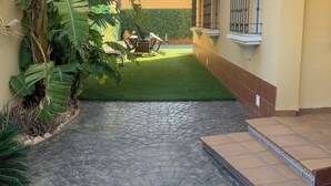 Ein gepflasterter Innenhof mit einem kleinen Pool, umgeben von einem gelben Gebäude mit einem Ziegeldach und einer grünen Hecke.