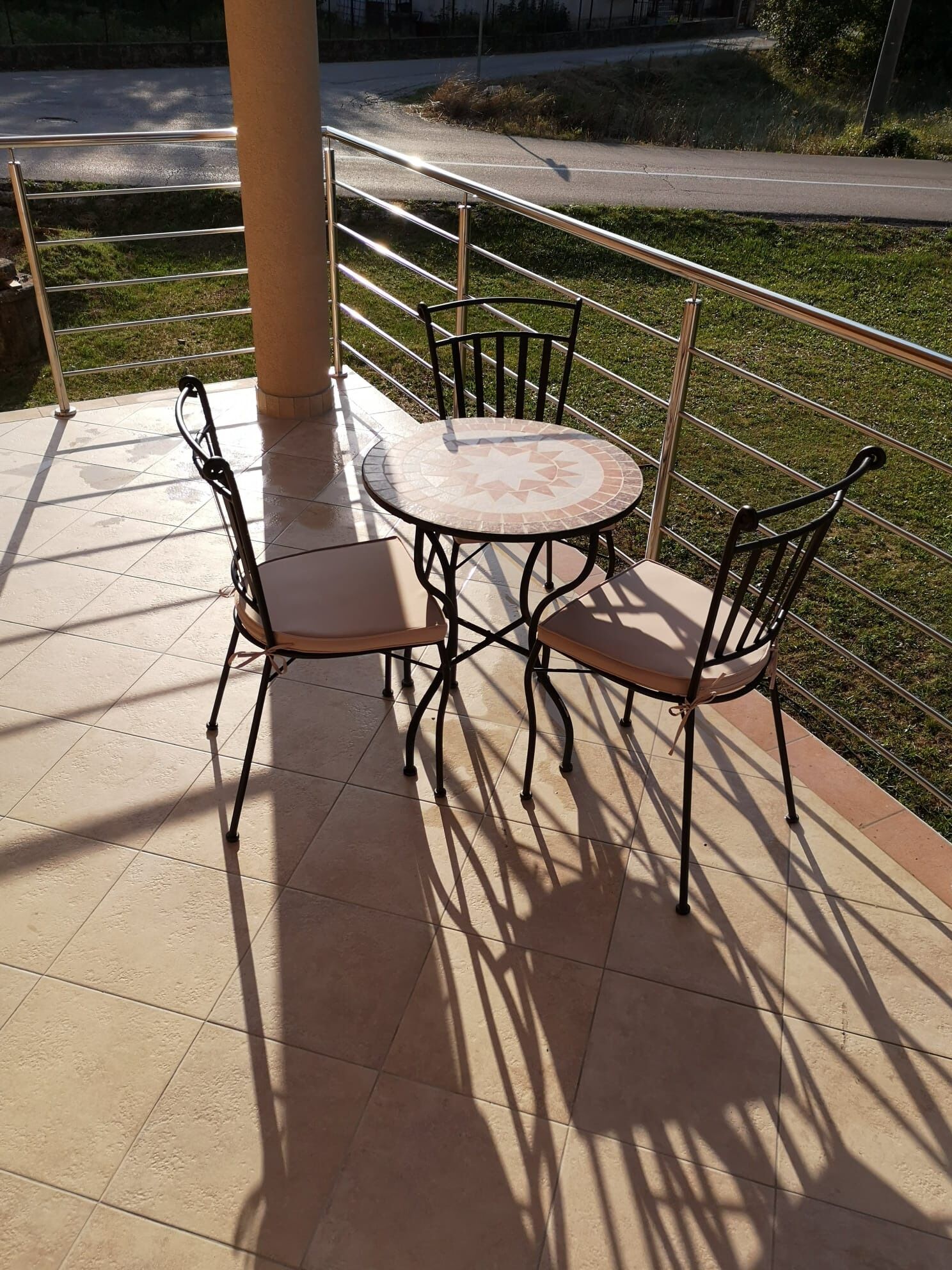 Une table ronde entourée de quatre chaises, sur une terrasse carrelée.