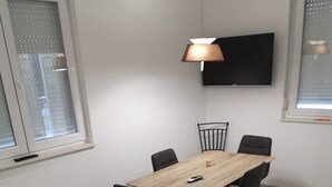 A modern living room with a wooden dining table, black chairs, a brown sofa with yellow cushions, a small round side table, and a mounted TV. - Apartman Sea Lake Magic 2 (Vinodol)