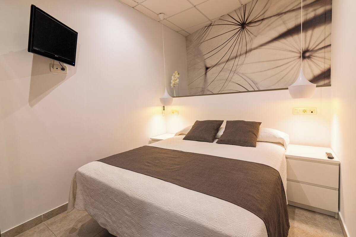 Une chambre à coucher bien aménagée, avec un lit, des tables de chevet, un téléviseur fixé au mur et un miroir décoratif.