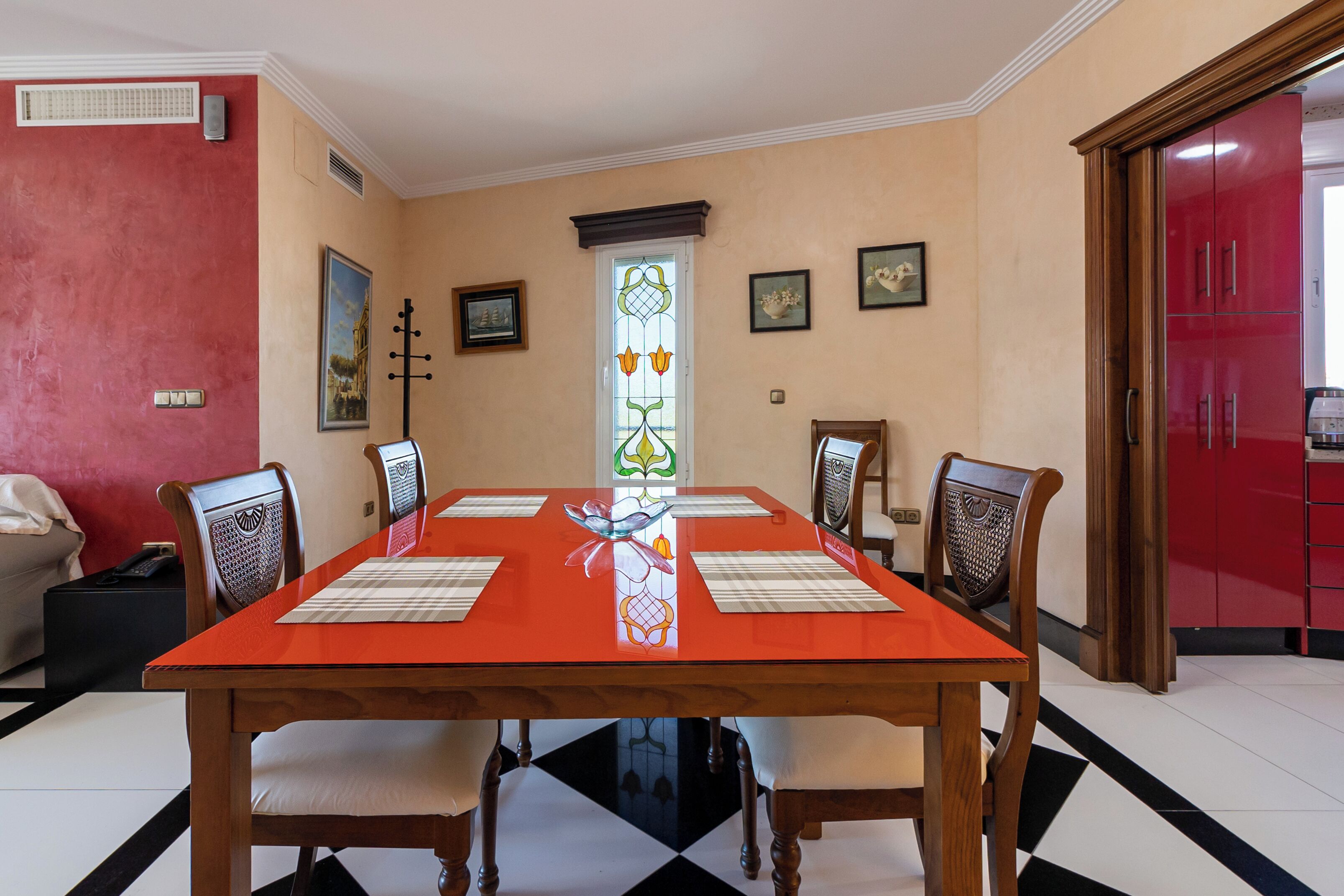 A dining room with a rectangular table, four chairs, a red cabinet, and a decorative glass window.