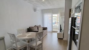 Una sala de estar moderna con un sofá, una mesa de comedor con sillas y una zona de cocina con refrigerador.