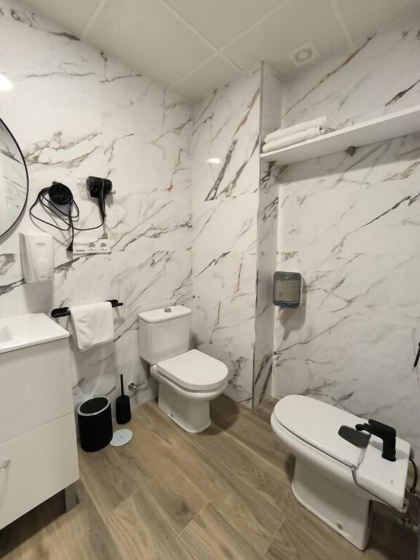 A bathroom with marble walls, a toilet, a bidet, and a sink.