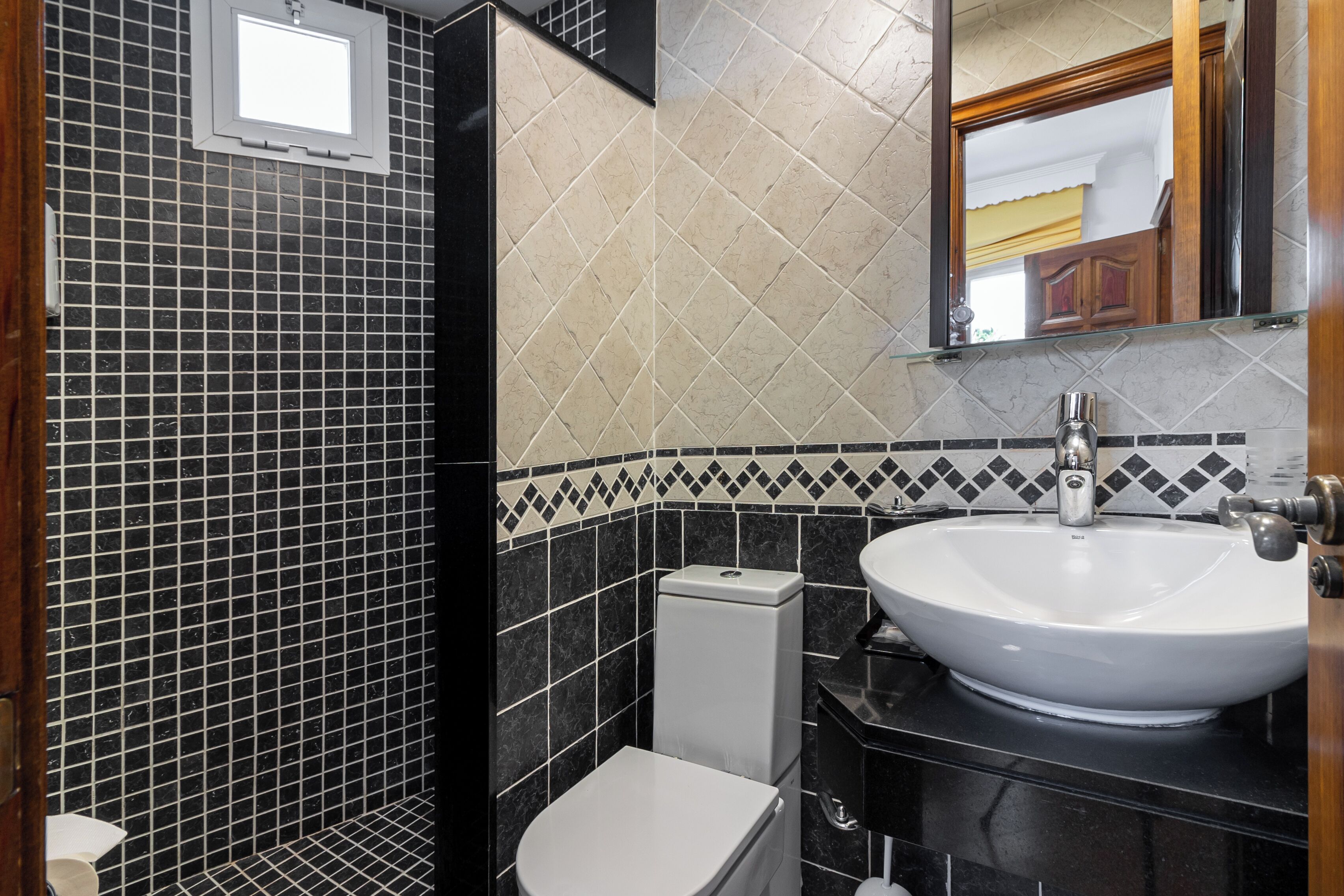 Ein Badezimmer mit schwarzem und beigem Fliesenbelag, einem weißen Waschbecken und einer Toilette.