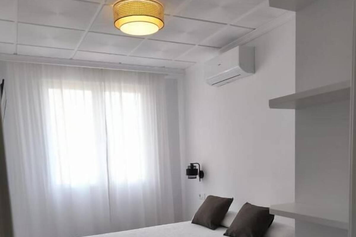 Une chambre à coucher moderne avec un lit, un luminaire au plafond et une fenêtre avec des rideaux.
