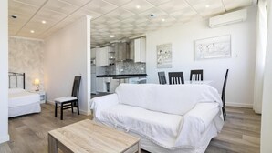 Una sala de estar moderna con un sofá blanco, una mesa de centro de madera y un comedor con una mesa y sillas blancas.