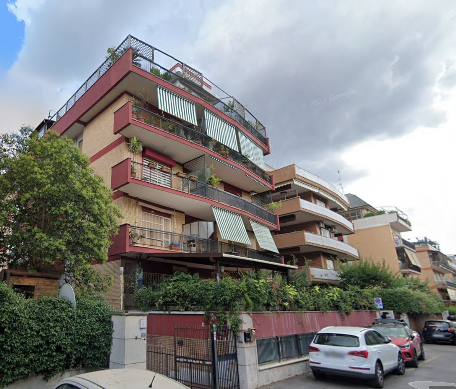 A multi-story residential building with balconies, a gated entrance, and parked cars.