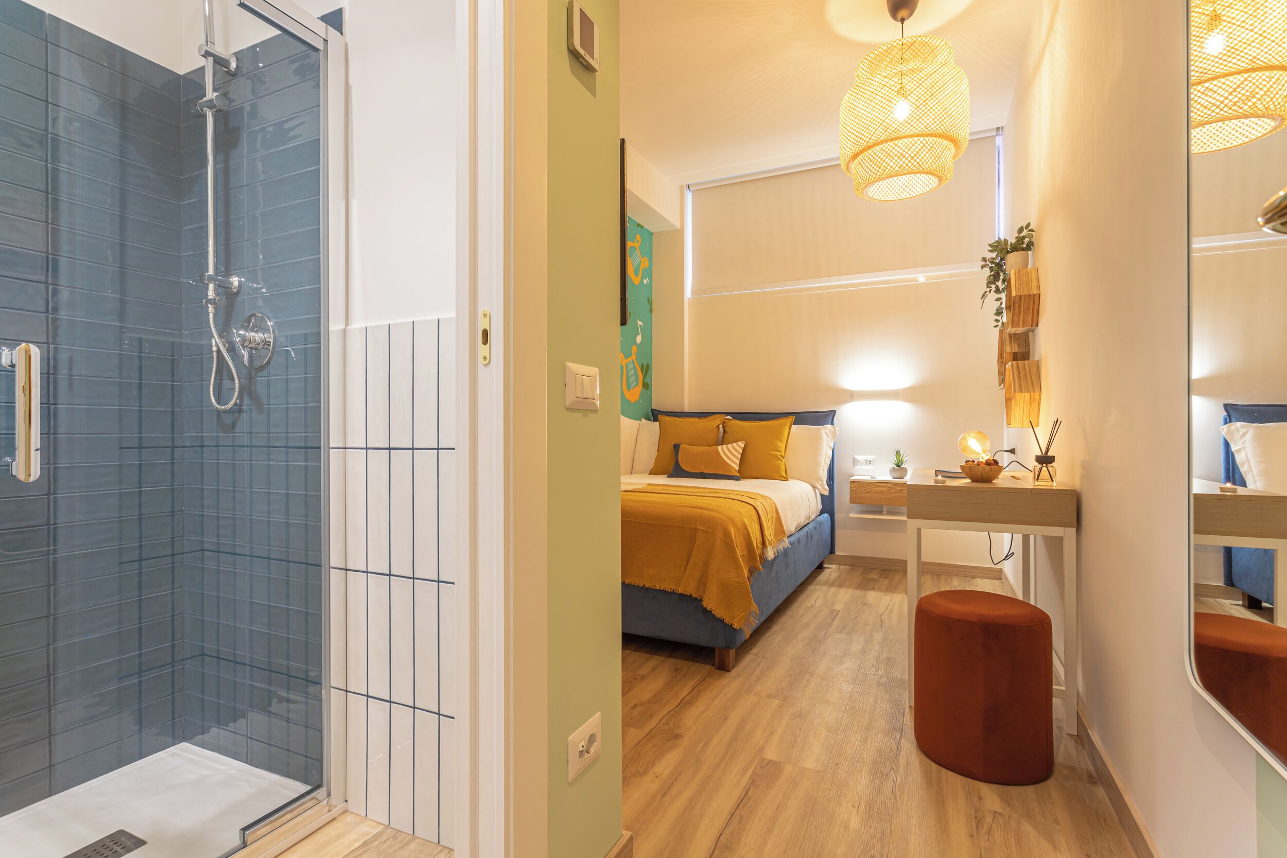 Un baño moderno con ducha, una cama con cabecera azul, suelo de madera y un taburete pequeño.